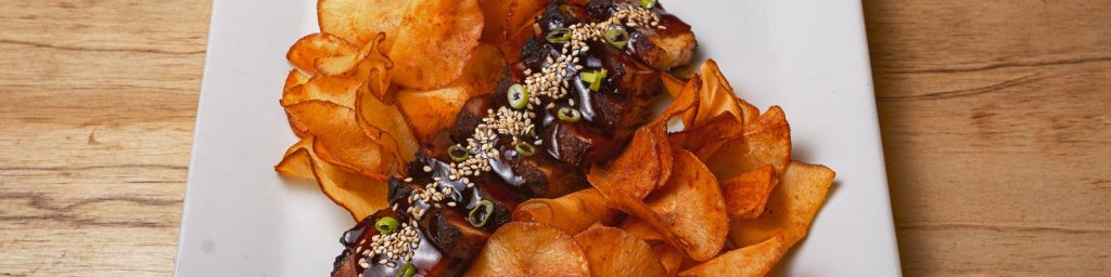 Cerdo a la brasa con corteza crujiente, salsa, sésamo y cebolleta junto a chips artesanos — restaurante de carne a la brasa en Barcelona centro, ComePorketa Eixample