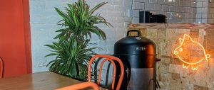 Interior de ComePorketa en el Eixample de Barcelona: ahumador a la vista, sillas naranjas y neón del cerdito, sala de fast casual